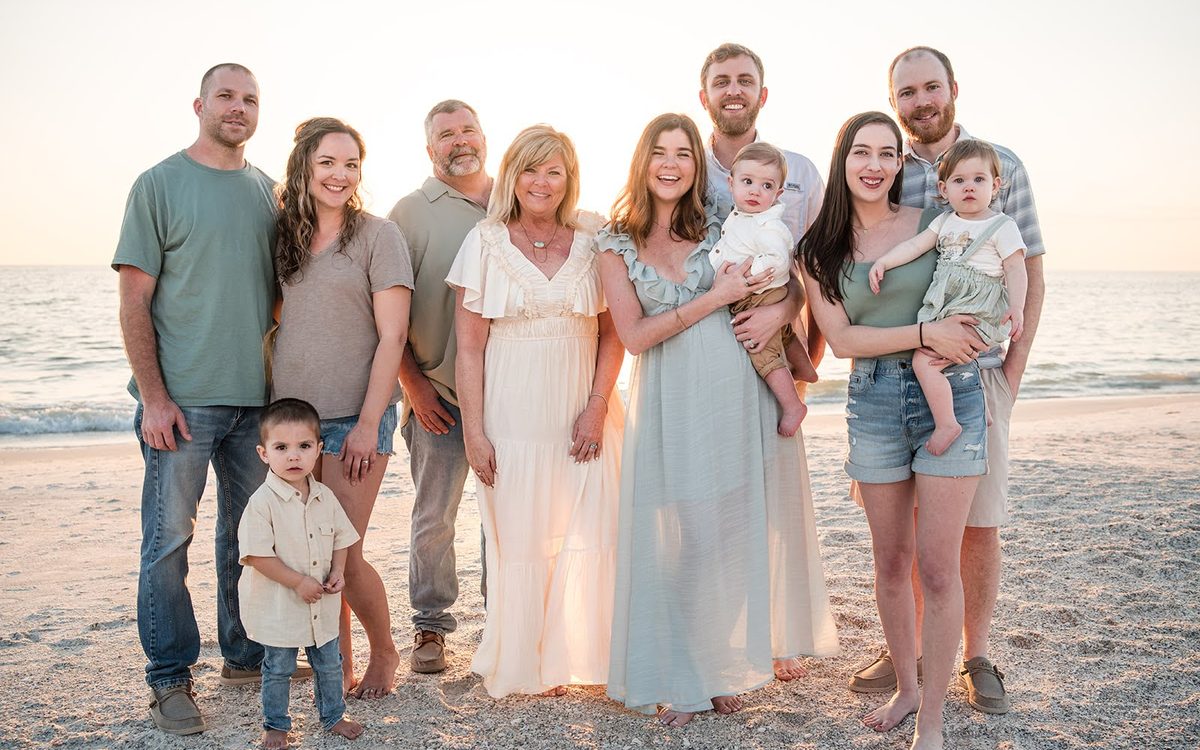Extended family of ten in coordinated neutrals photographed on the beach at sunset