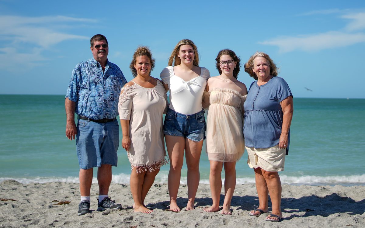 Family of five standing barefoot on white sand with turquoise Gulf water behind them