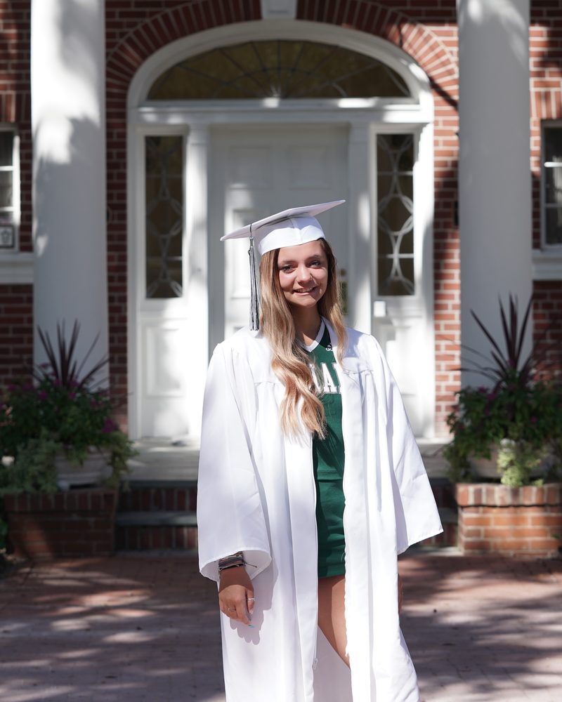 Graduate in a white cap and gown photographed outside a red brick building