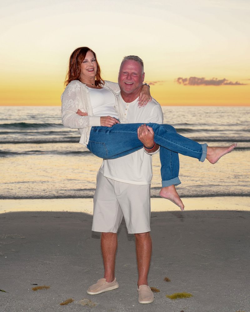 Laughing couple, one carrying the other along the shoreline at sunset on a Gulf Coast beach in Florida