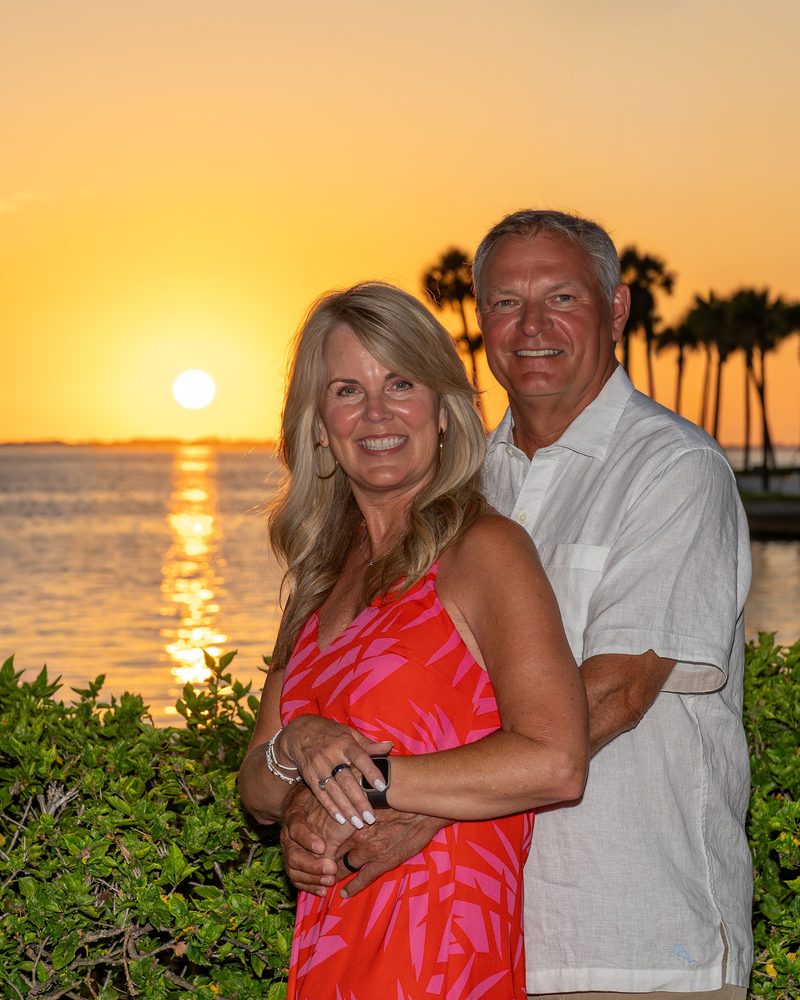 Couple embracing at sunset with palm trees and the water behind them in Sarasota, Florida