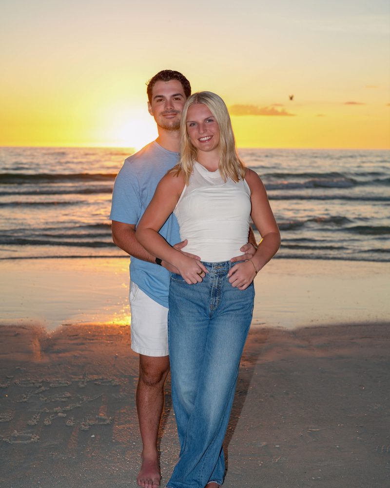 Young couple standing barefoot on the wet sand as the sun sets over the Gulf of Mexico