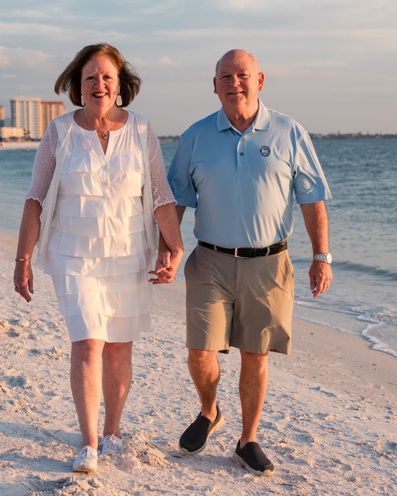Couple holding hands as they walk along the water's edge on a white sand beach in the late afternoon