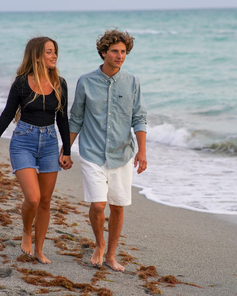Couple walking barefoot along the tideline holding hands with the surf beside them